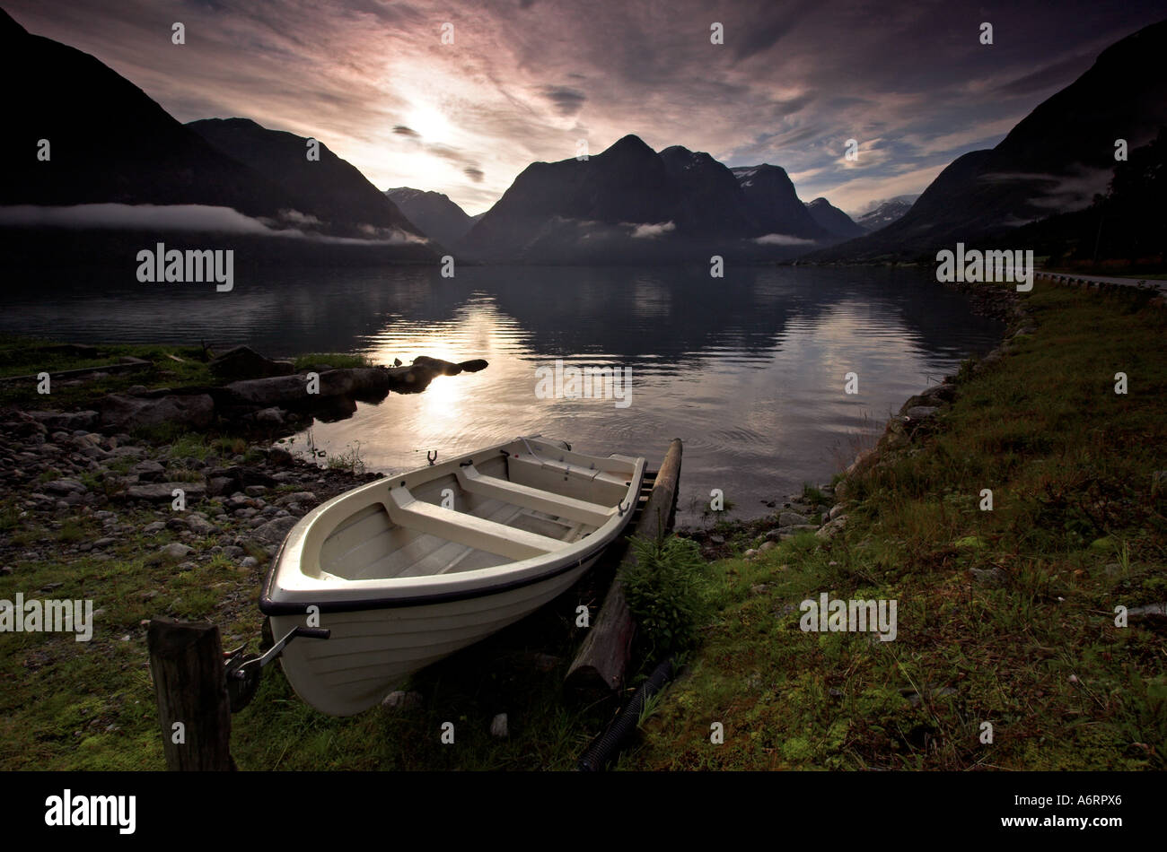 Ein kleines Boot am Ufer von einem norwegischen Fjord angebunden.  Niedrige Strähnen Wolke hängen über den stillen Wassern Stockfoto