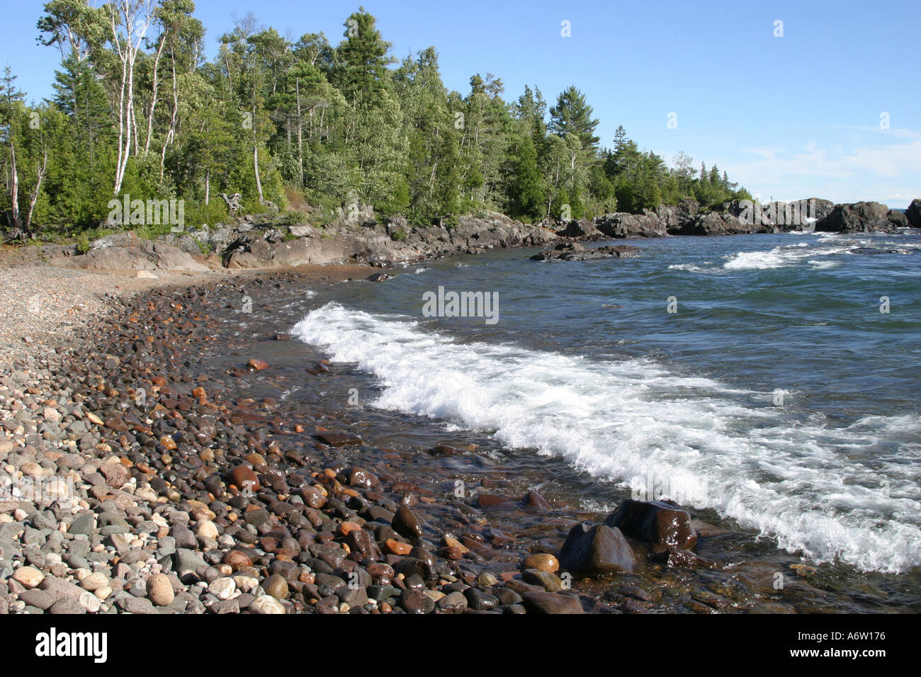 Wasser waschen auf felsigen Strand mit Bäumen im Hintergrund Stockfoto
