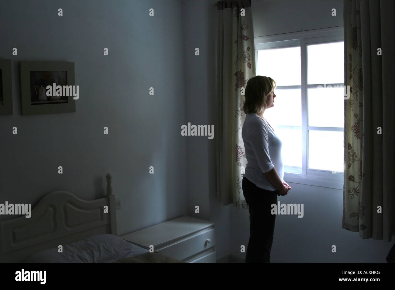 traurige Frau, Blick aus dem Schlafzimmerfenster Stockfoto