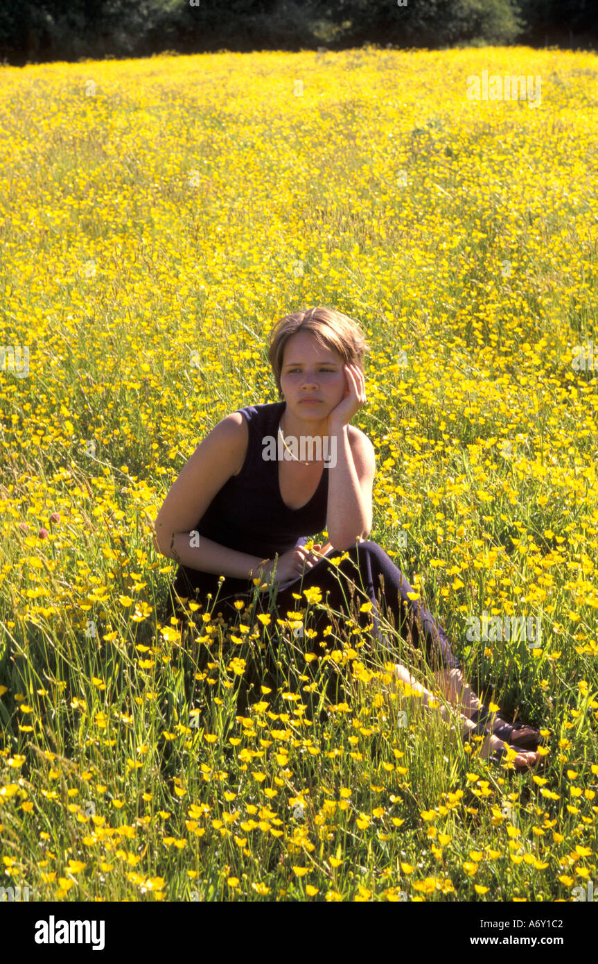 Teenager-Mädchen suchen wehmütig traurig und nachdenklich allein in einem Feld von herrlichen gelben Butterblumen in UK Sommer Landschaft Stockfoto