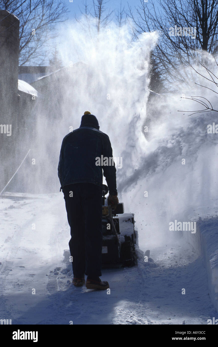 Minnesota Mann Snowblowing Winter Sturm Schnee Gebäude Baum Zweige zurück Stockfoto