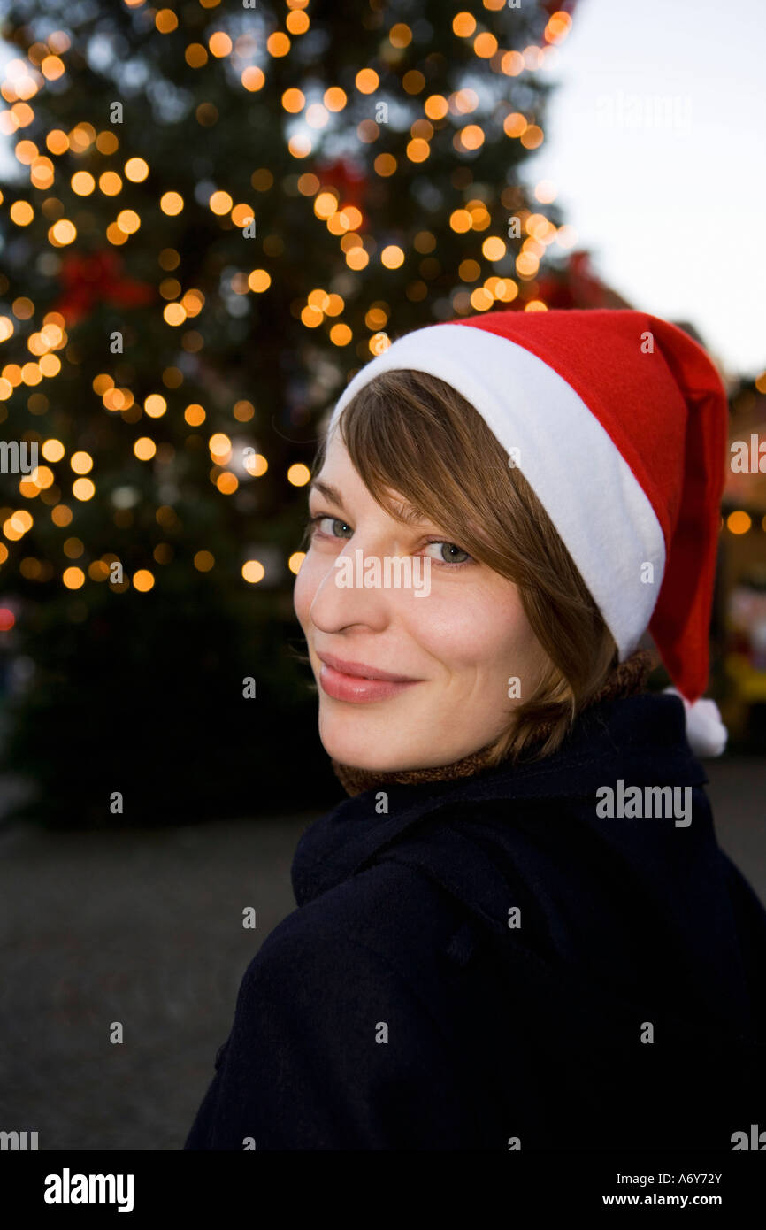 Frau trägt eine Weihnachtsmütze vor einem Weihnachtsbaum Stockfoto