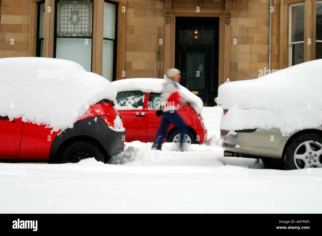 Frau mit roter Jacke Wandern in starkem Schneefall zwischen parkenden Autos Stockfoto