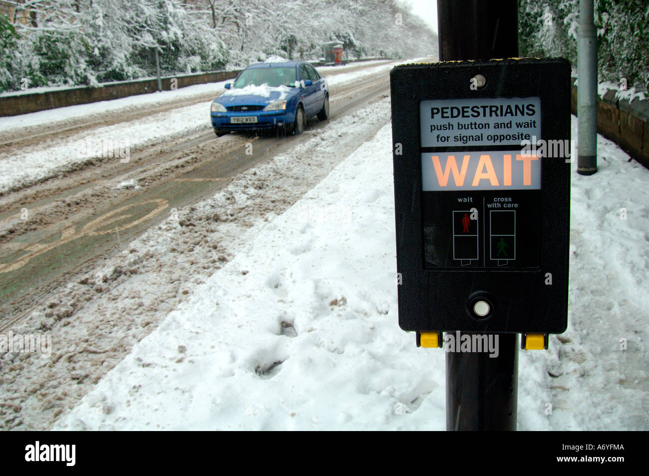 Straße überqueren Fußgänger warten Zeichen mit Auto vorbei in gefährlichen winterlichen Bedingungen beleuchtet Stockfoto