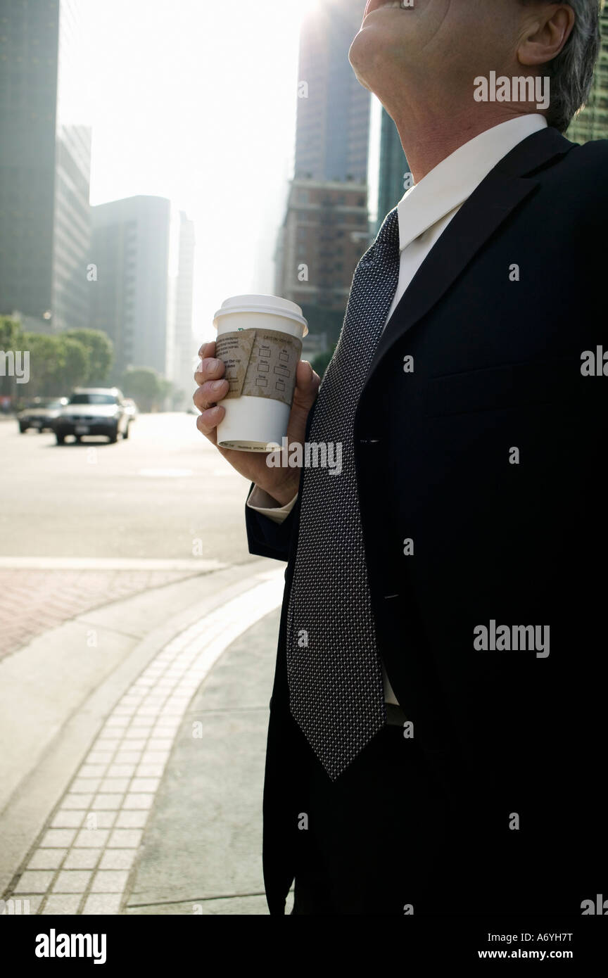 Geschäftsmann stand an einer Straßenecke hält eine Tasse Kaffee Stockfoto