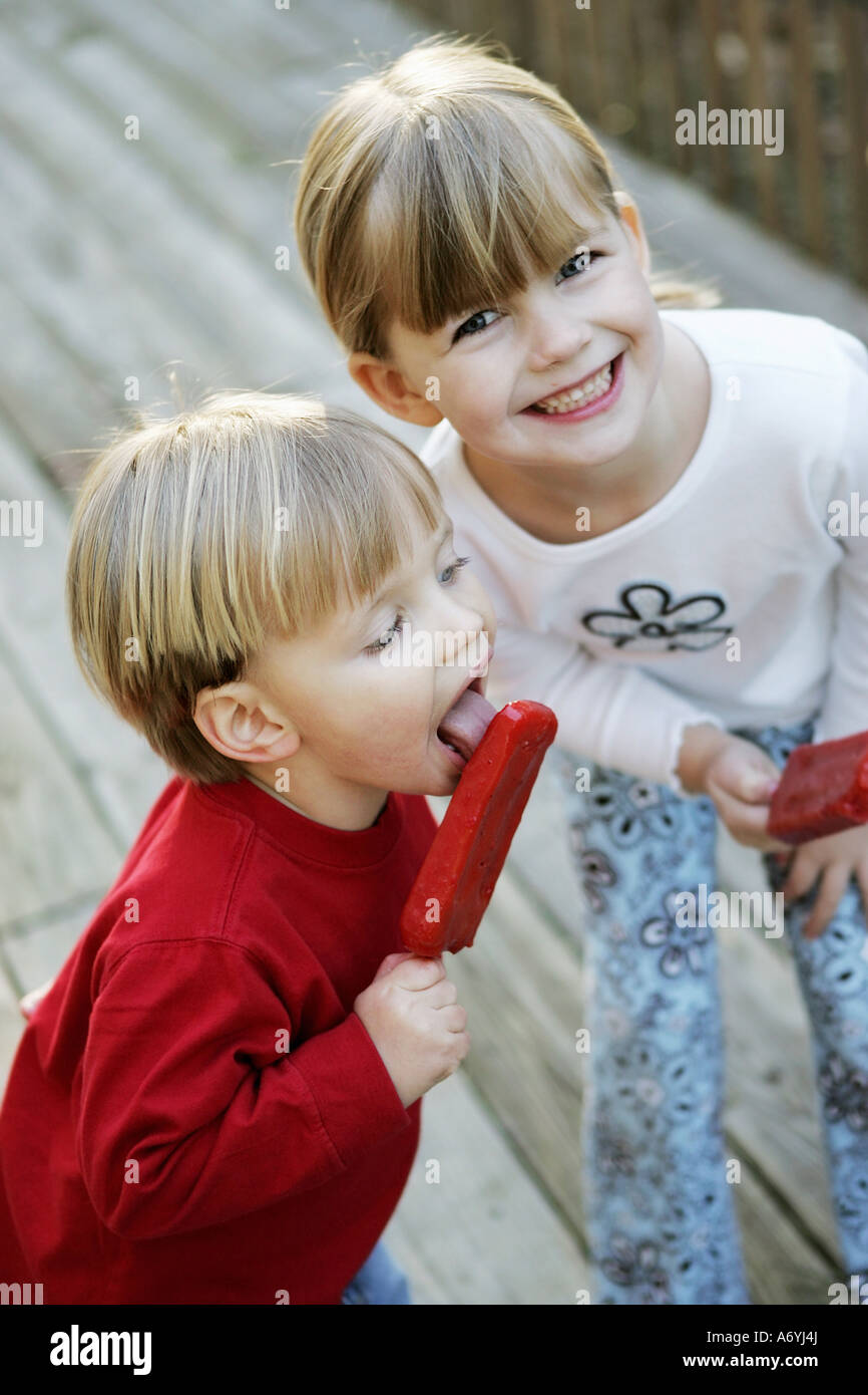 Ein Junge und ein Mädchen essen Eis am Stiel in einem Hinterhof Stockfoto