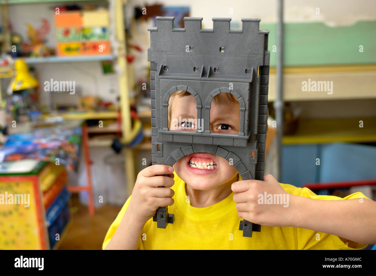 Kleiner Junge Grimassen hinter seinem Spielzeug Ritterburg Stockfoto