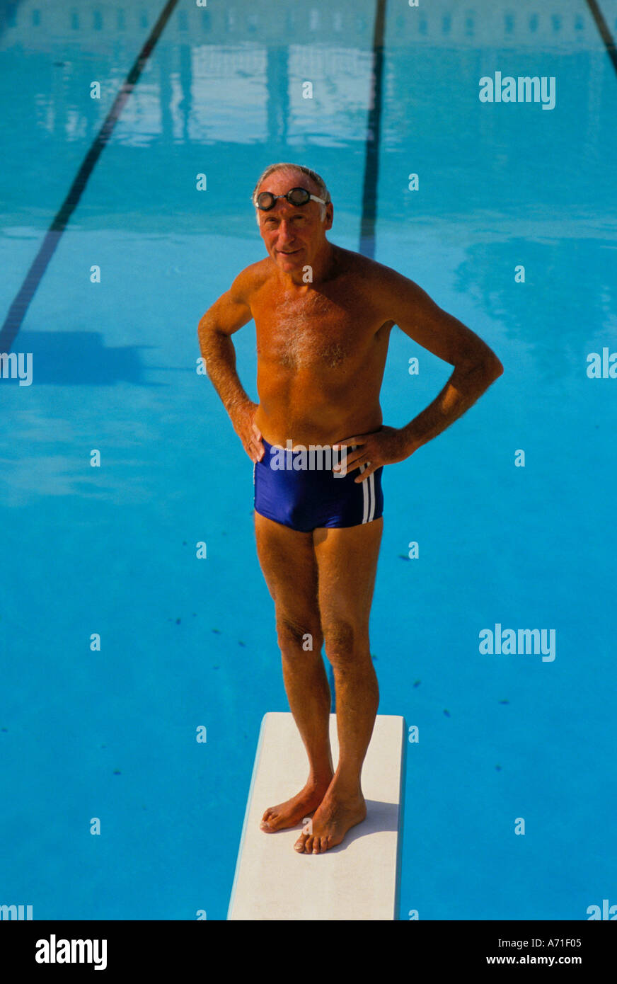 Gebräunt und Fit senior Mann trägt blaue Badehose und ein paar Brillen, stehend auf einem Sprungbrett über einen Swimming pool Stockfoto