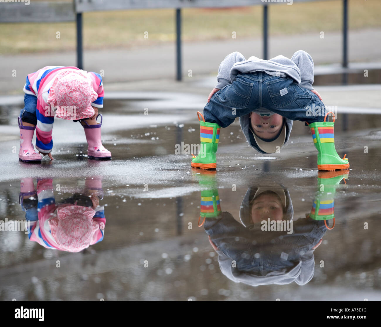 Zwei kleine Kinder spielen in der Pfütze, die Spiegelungen im Wasser betrachten Stockfoto