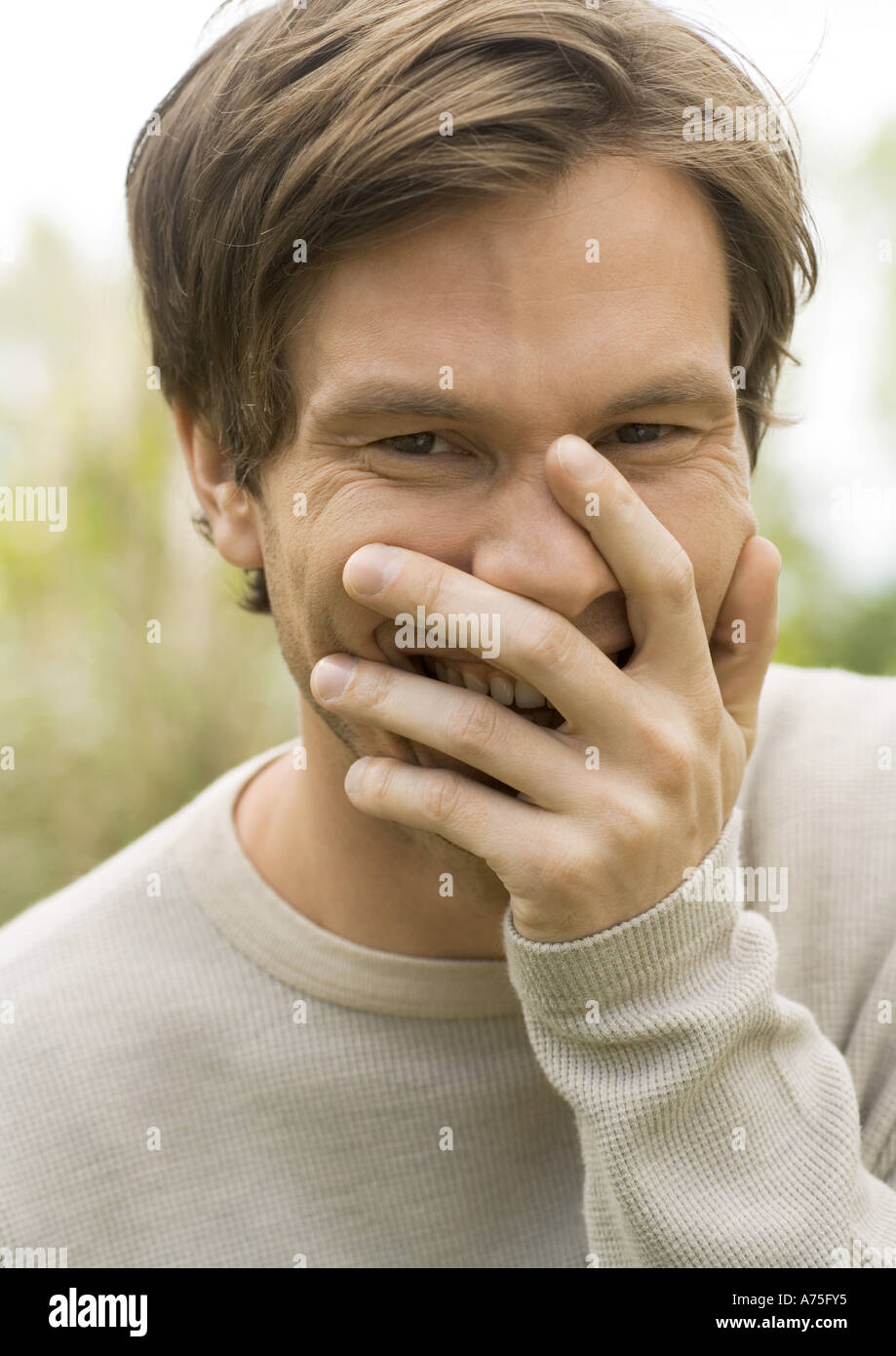 Junger Mann, lachend und den Mund mit der Hand, Porträt Stockfoto
