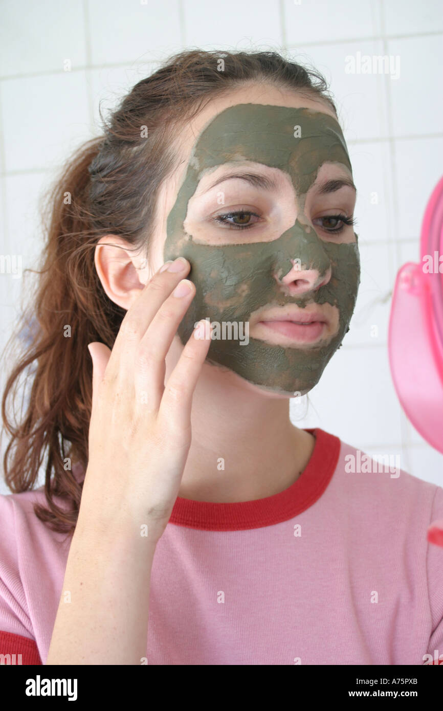 Teenager auf der Suche in einem Spiegel während der Anwendung eine Moorpackung Stockfoto