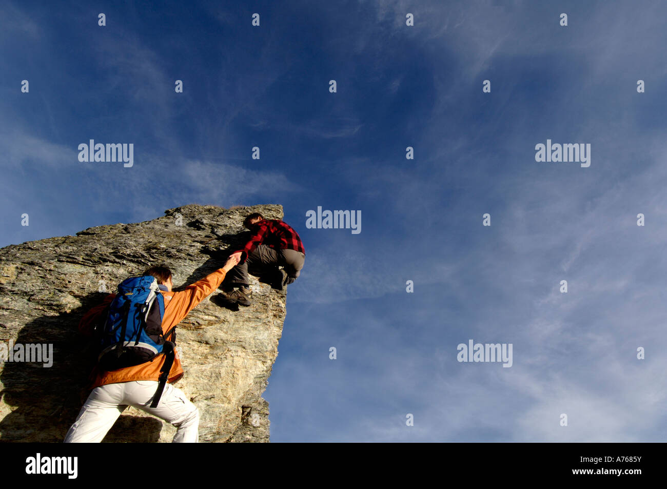 Junges Paar Klettern auf Berggipfel, Mann Rückansicht hilft Frau, Stockfoto