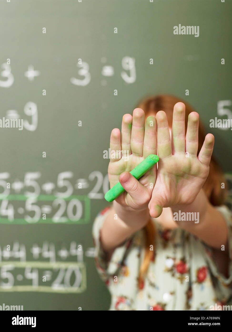 Mädchen (6-7) stehend von Blackboard und Verkleidung Face mit Händen, Nahaufnahme Stockfoto