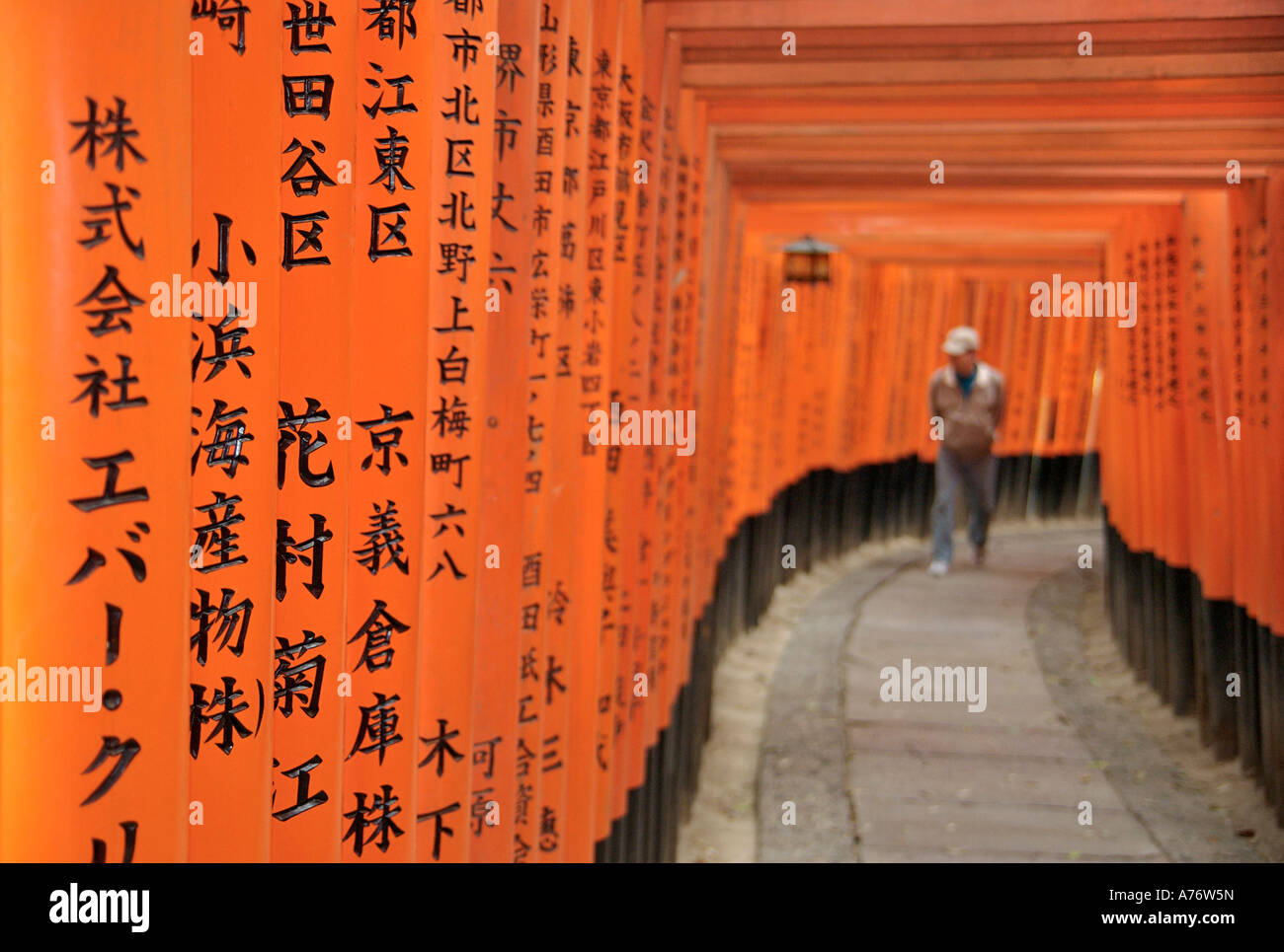 Orange lackiert Torii-Tore im Fushimi Inari-Taisha-Schrein in Kyoto Japan Kanji geschrieben Beiträge Walkng Mann im Bokeh jenseits Stockfoto