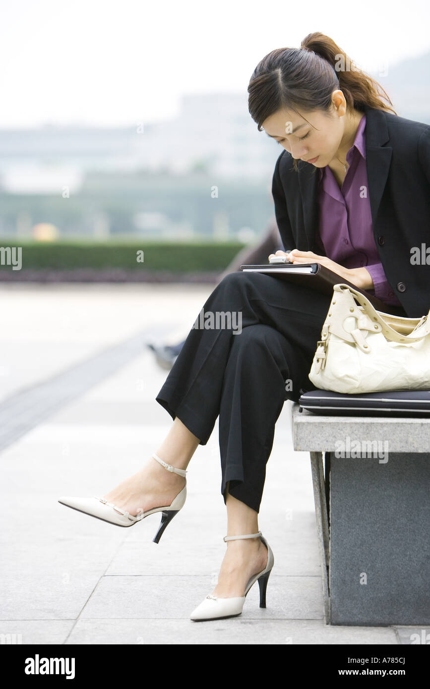 Junge Geschäftsfrau sitzen auf Bank blickte auf Handy Stockfoto