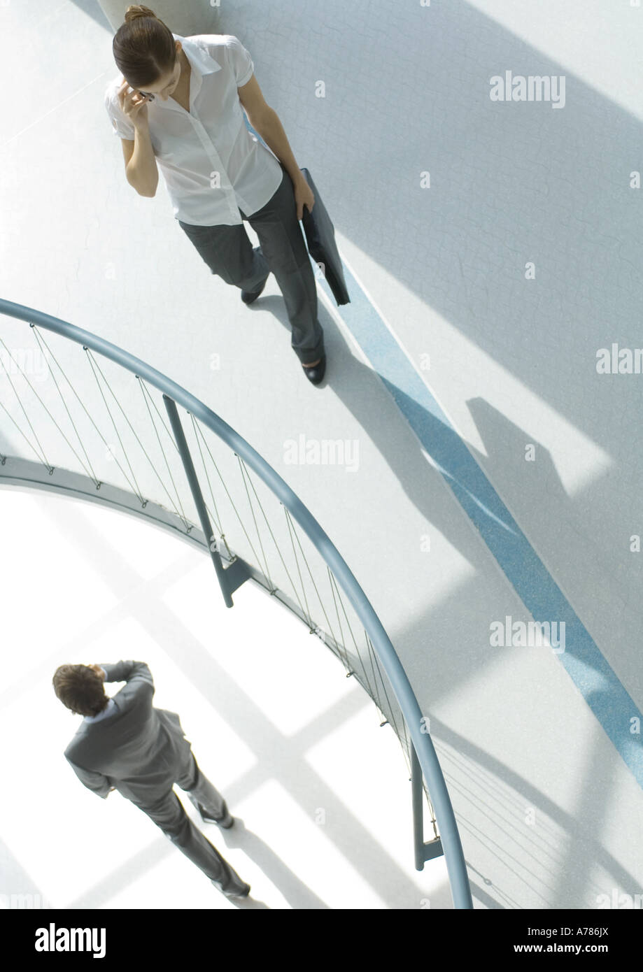 Frau mit Handy in der Nähe von Geländer, Untergeschoss, Geschäftsmann zu Fuß mit Handy, erhöhte Ansicht Stockfoto