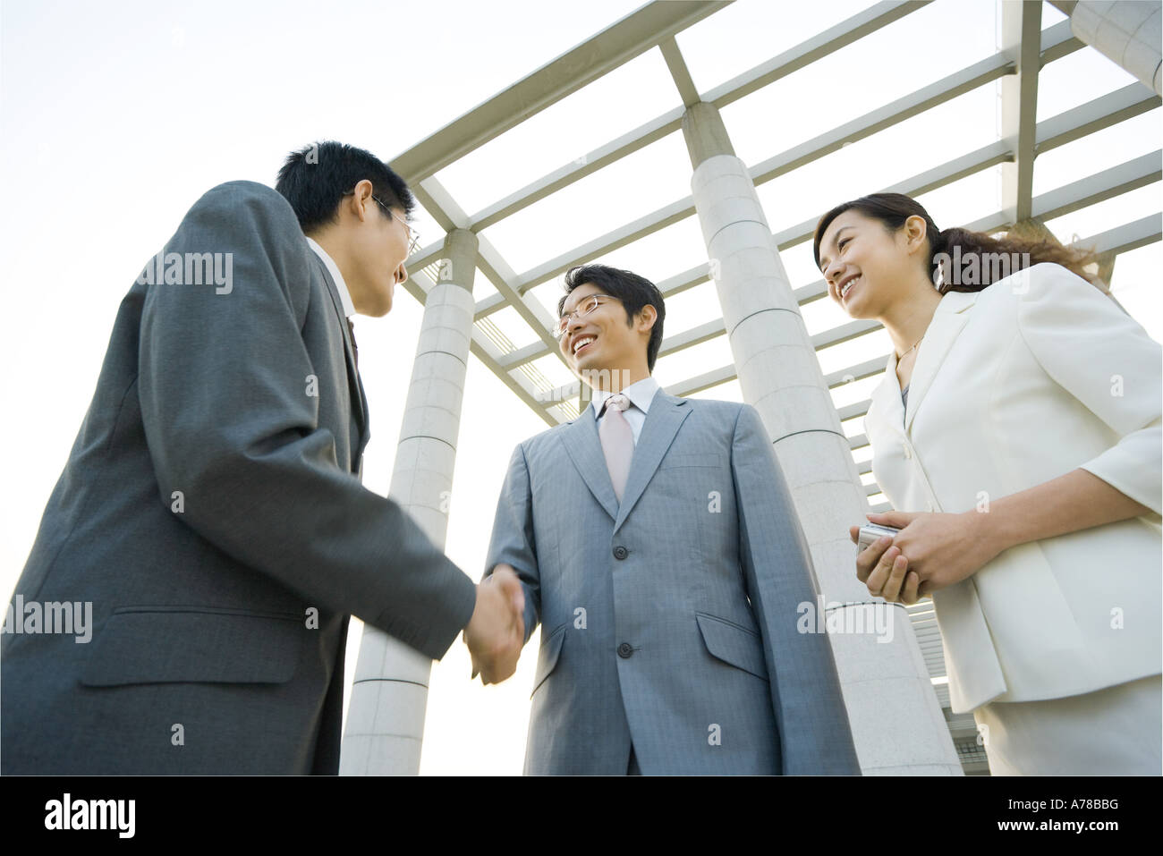 Zwei Geschäftsleute, die Hände zu schütteln, während Geschäftsfrau in der Nähe, niedrigen Winkel Ansicht steht Stockfoto