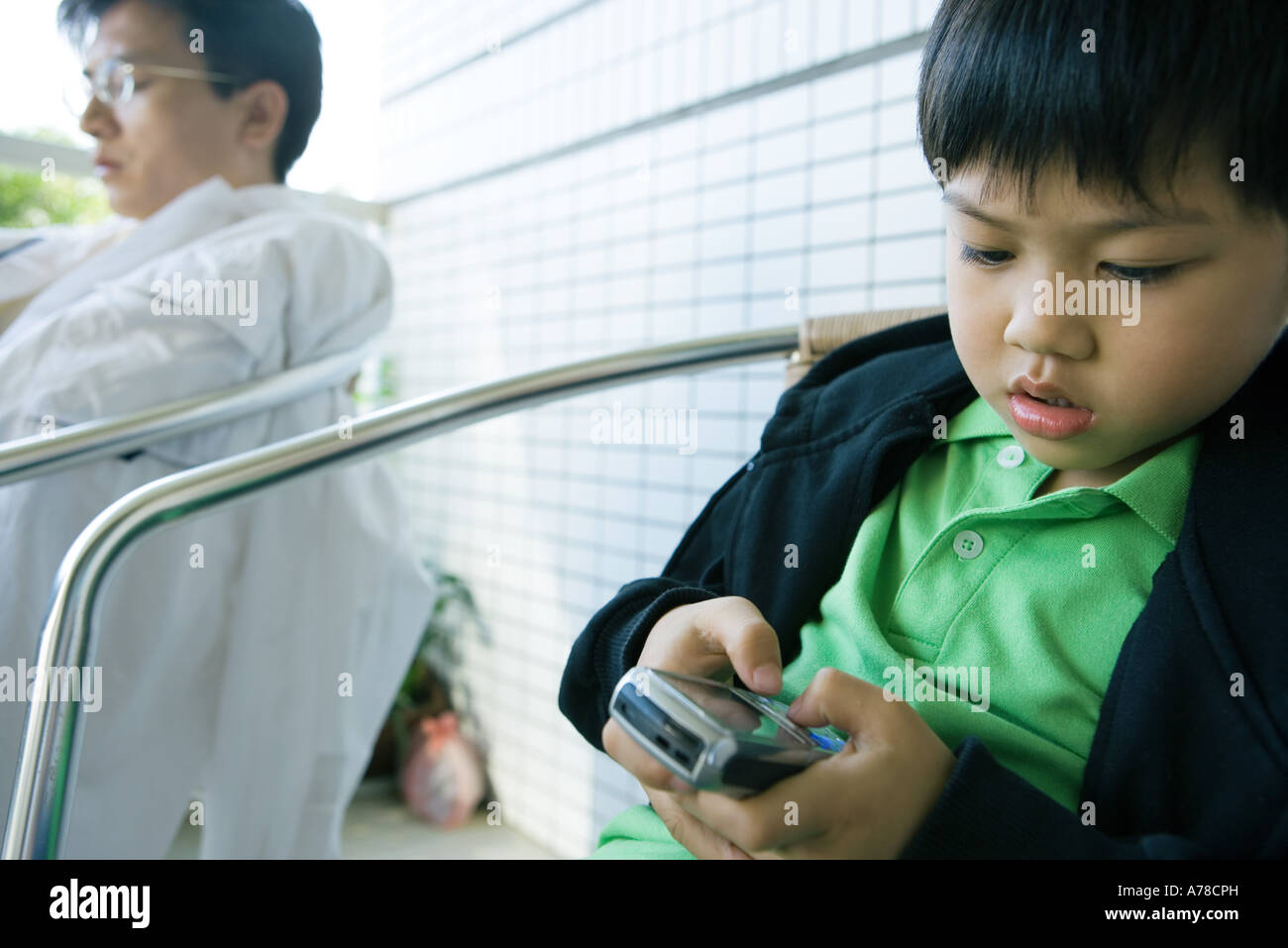 Junge mit Handy, während Vater mit geschlossenen Augen sitzt Stockfoto