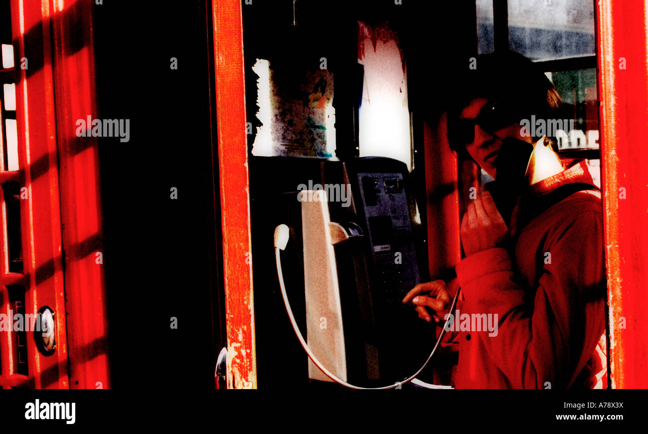 LADY IN RED PHONEBOX.  Junge Ausländerin in einer Call-Box, erschossen behandelt zu einem produzieren kiesig, körnig, hart Bild. Stockfoto