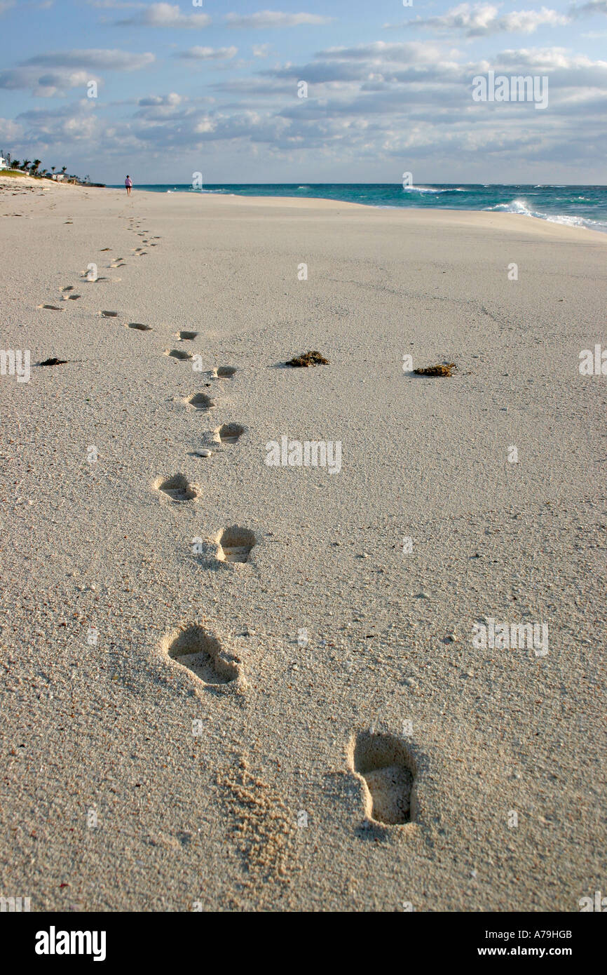 Einsame Strandwanderung. Eine lange Reihe von tiefen Fußspuren im Sand führen zu einer kleinen Figur allein auf eine topische Strand zu Fuß Stockfoto