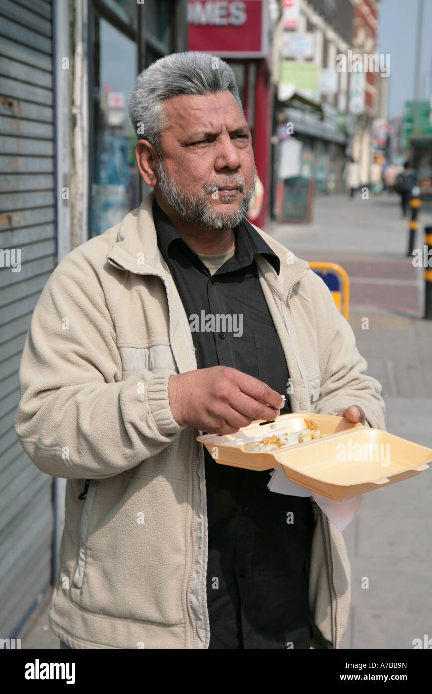 Asiatischer Mann Essen Speisen zum mitnehmen in Tooting, London Stockfoto