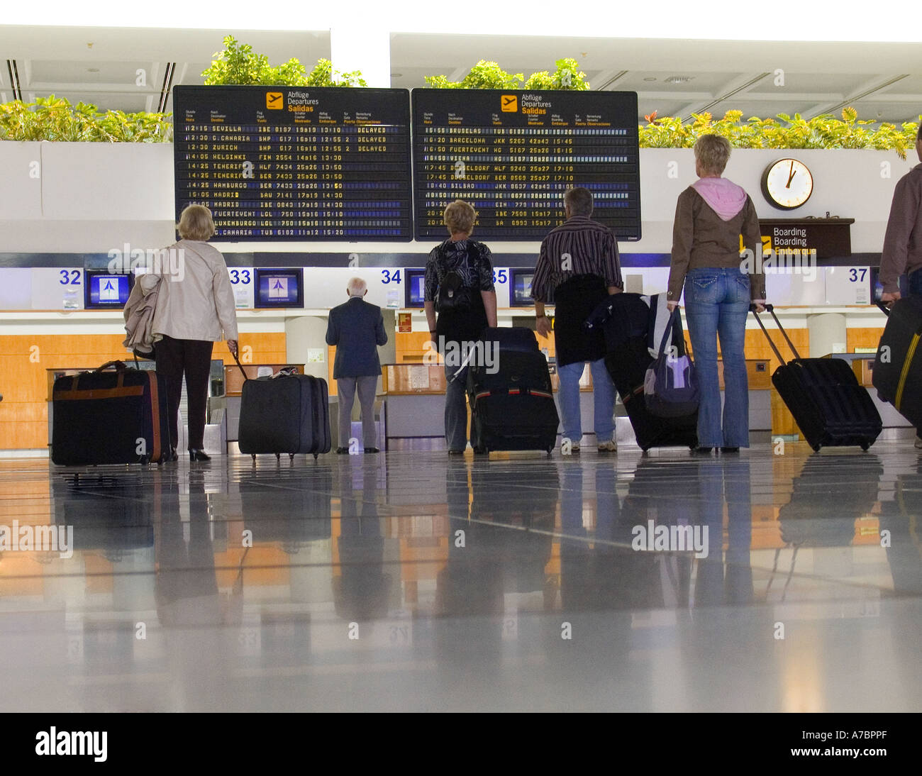 ABFLUGPASSAGIERE Flughafenpassagiere waren auf der modernen Konkurshalle sozial distanziert und schauten sich die Informationsbildschirme zu den Abflugzeiten im Flughafenterminal an Stockfoto