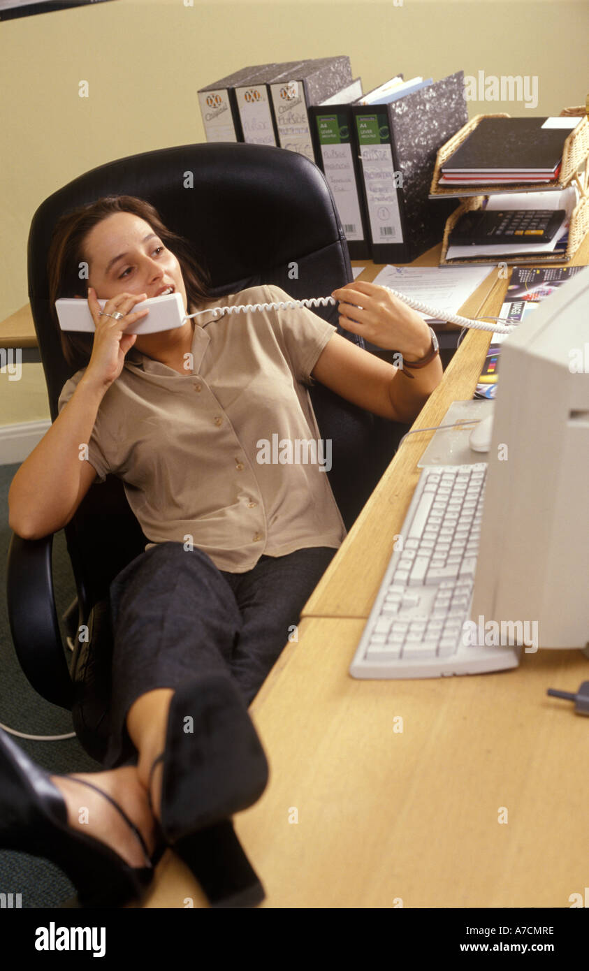 Frau am Telefon im Büro mit Füßen auf Schreibtisch Stockfoto