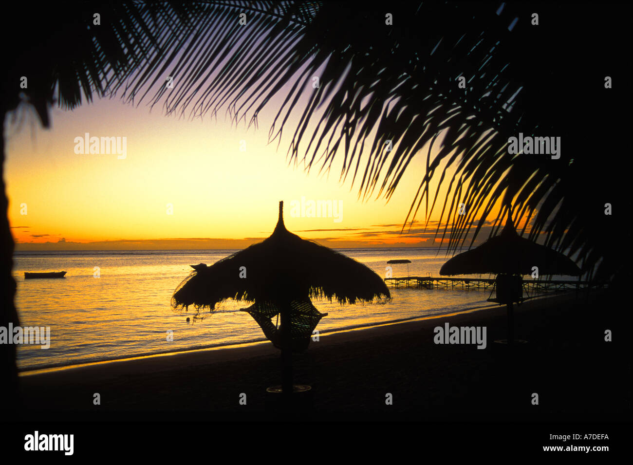 Indischer Ozean Sonnenuntergang mit Boot und Steg, Meer, Silhouetten von palmenblättern Overhead und polynesischen Stil vordächer am Strand, Wolmar, Mauritius Stockfoto