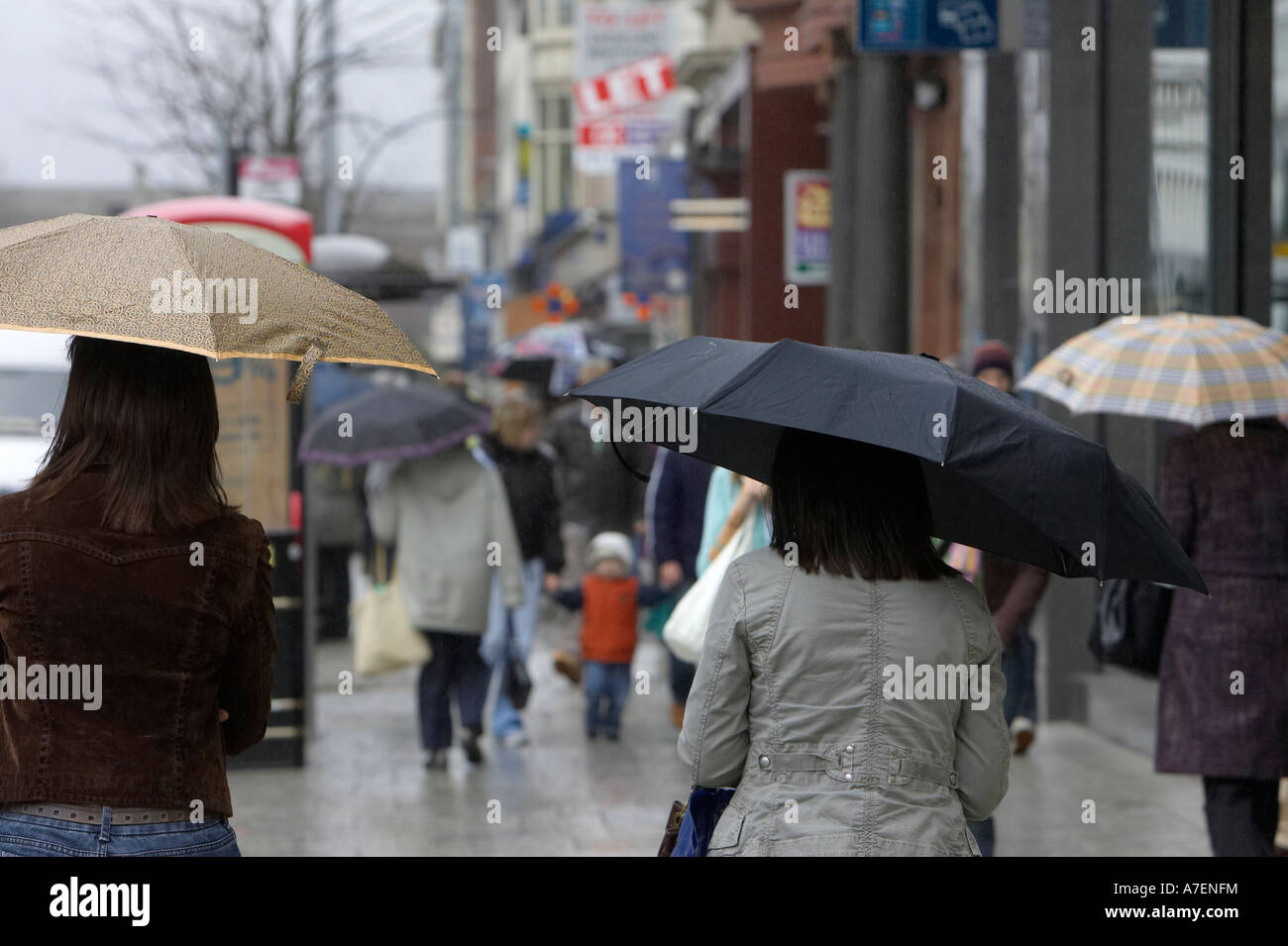 zwei junge Frauen, die Sonnenschirme, die hinunter einer nasse Einkaufsstraße im Stadtzentrum zu Fuß entfernt von der Kamera hautnah Stockfoto