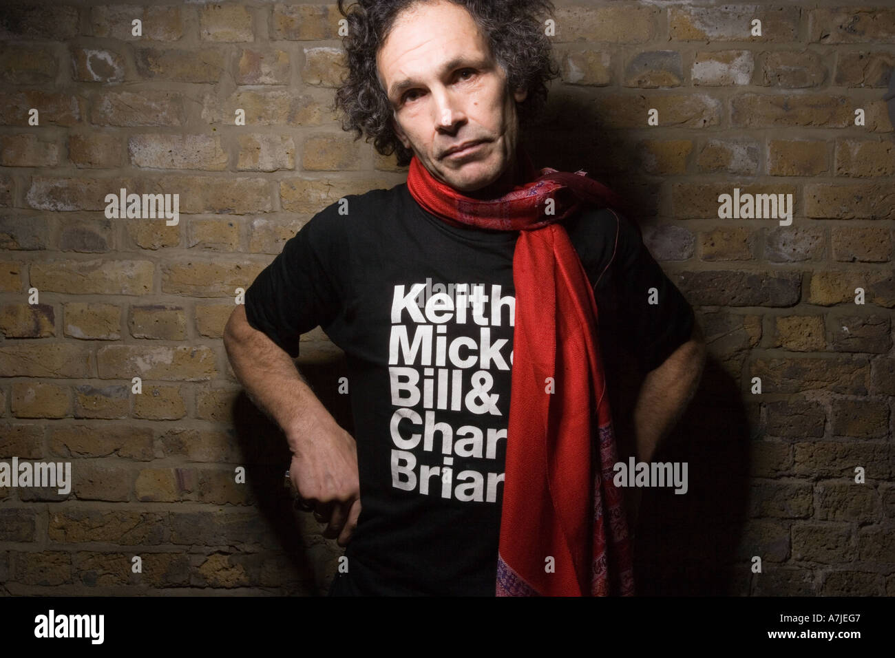 Ein Mann mittleren Alters in rolling stones T-shirt einer gemauerten Wand, mit einem verträumten Ausdruck, Keith Richard Doppel Stockfoto