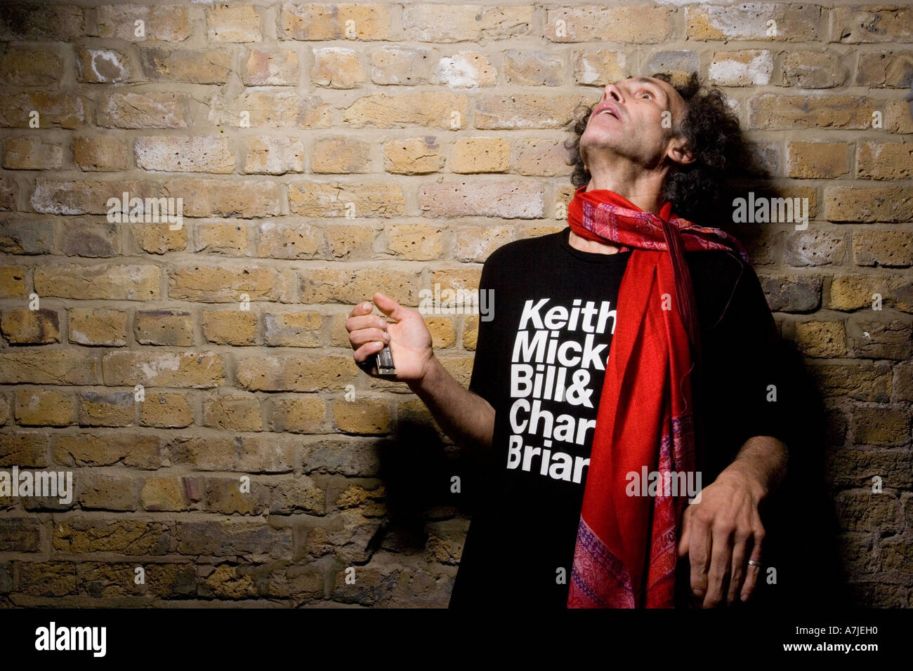 Ein Mann mittleren Alters in rolling stones T-shirt einer gemauerten Wand, mit einem verträumten Ausdruck, Keith Richard Doppel Stockfoto