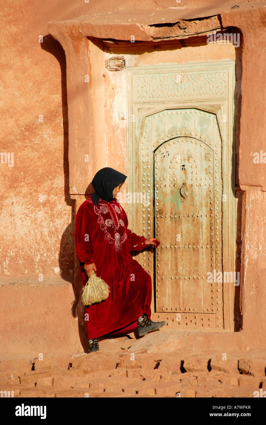 Frau im traditionellen Gewand gekleidet öffnet die alte Tür zu ihrem Haus aus Lehm Bou-Thrarar Marokko Stockfoto