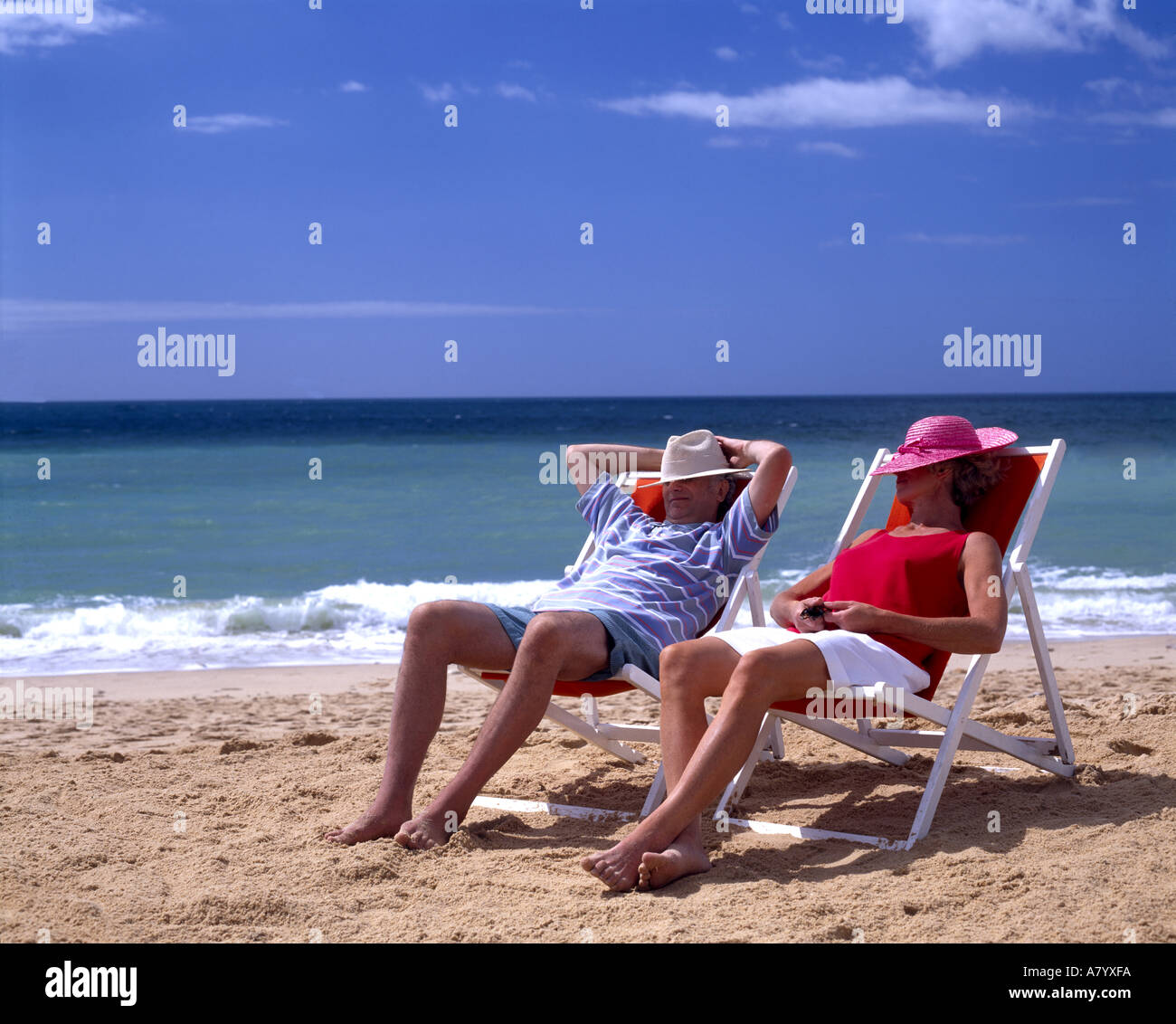 Paar mittleren Alters entspannen auf Liegestühlen tragen Hüte auf den Strand Stockfoto
