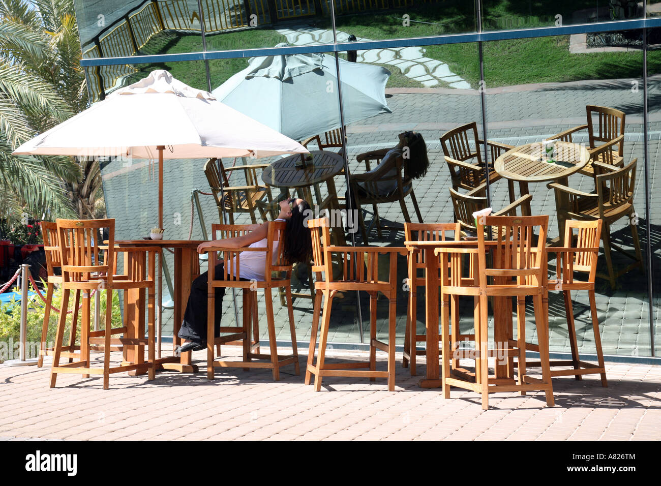 Ein junges Mädchen, ruht auf einem Stuhl unter einem Sonnenschirm in einem Straßencafé, Abu Dhabi, Vereinigte Arabische Emirate Stockfoto