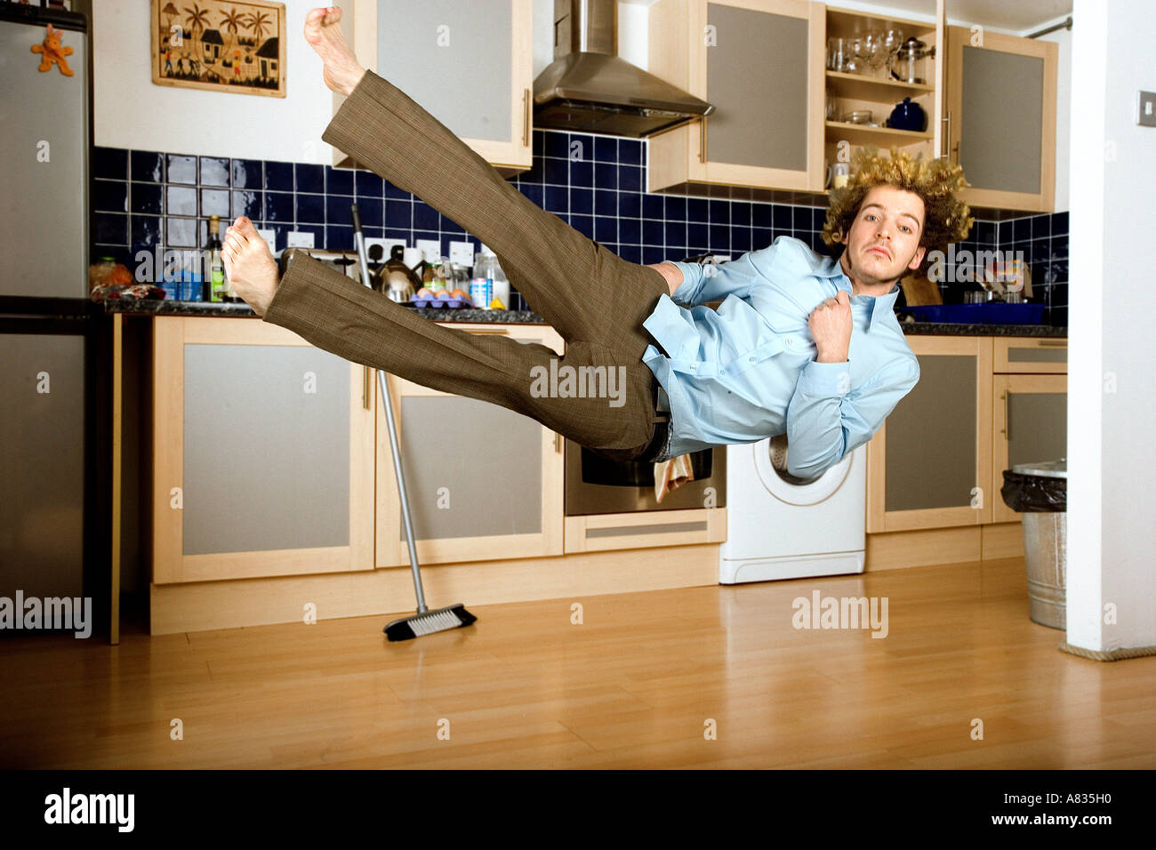 In der Luft junger Mann in Hose und Hemd in der Küche, die horizontal auf den Boden fällt Stockfoto