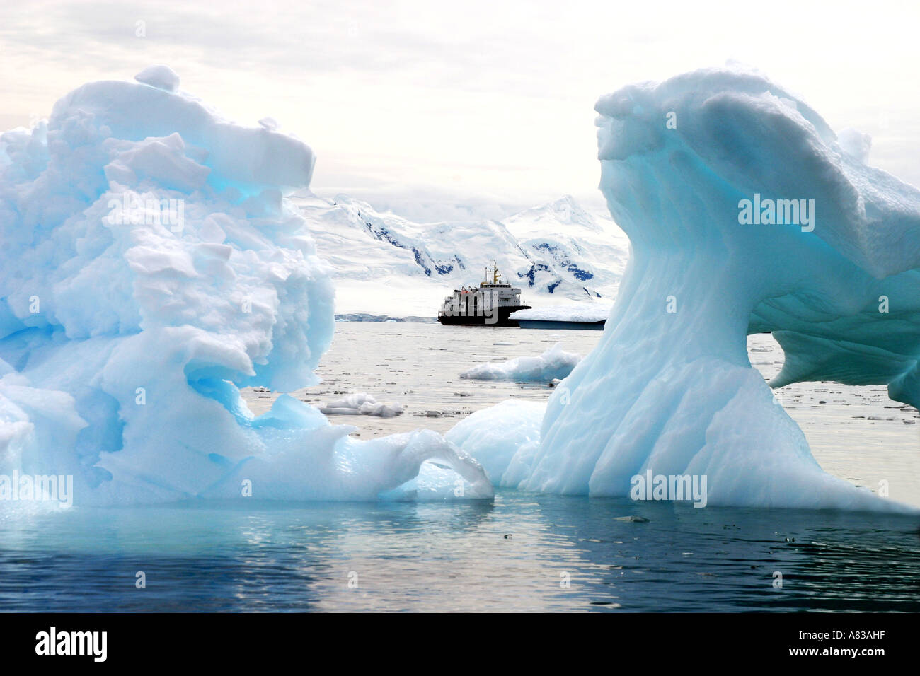 Eisbrecher-Kreuzfahrtschiff gesehen zwischen zwei farbige kleine Eisberge in der Antarktis. Stockfoto