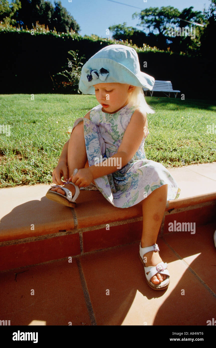 Kinder. Mädchen von 6 Jahren im Garten Handeln herauf Sandale Gurt. Stockfoto