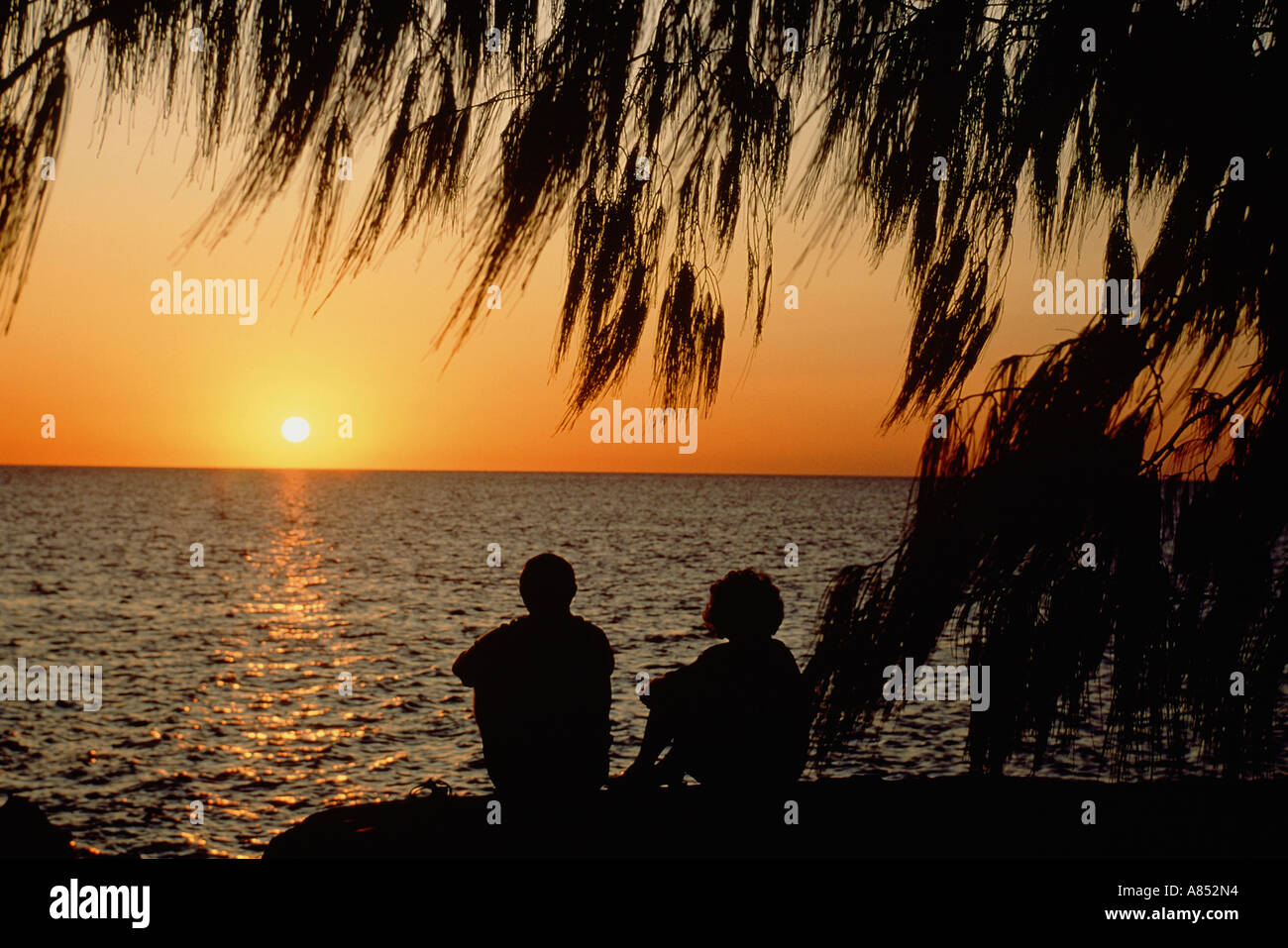 Australien. Queensland.  Silhouette eines Paares, die den Sonnenaufgang über dem Meer Horizont zu beobachten. Stockfoto