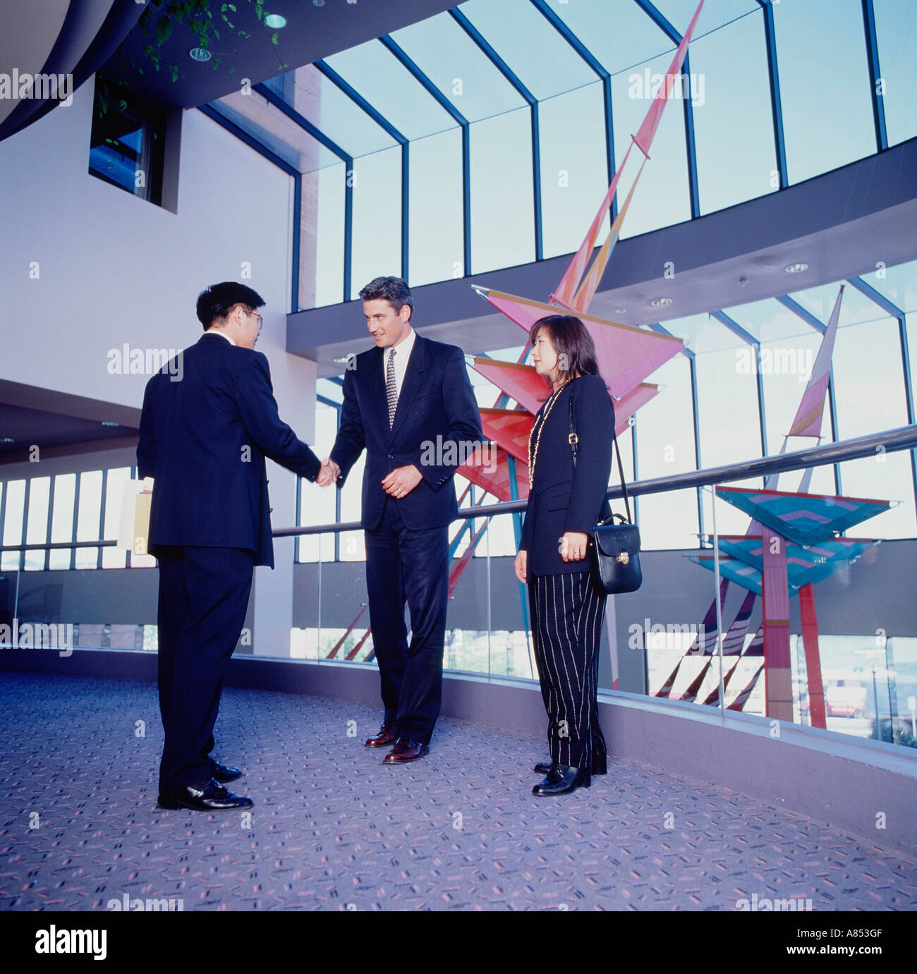 Zwei Männer und Frau stehend indoor Hochparterre modernen Geschäftshauses. Handshake-Gruß. Stockfoto