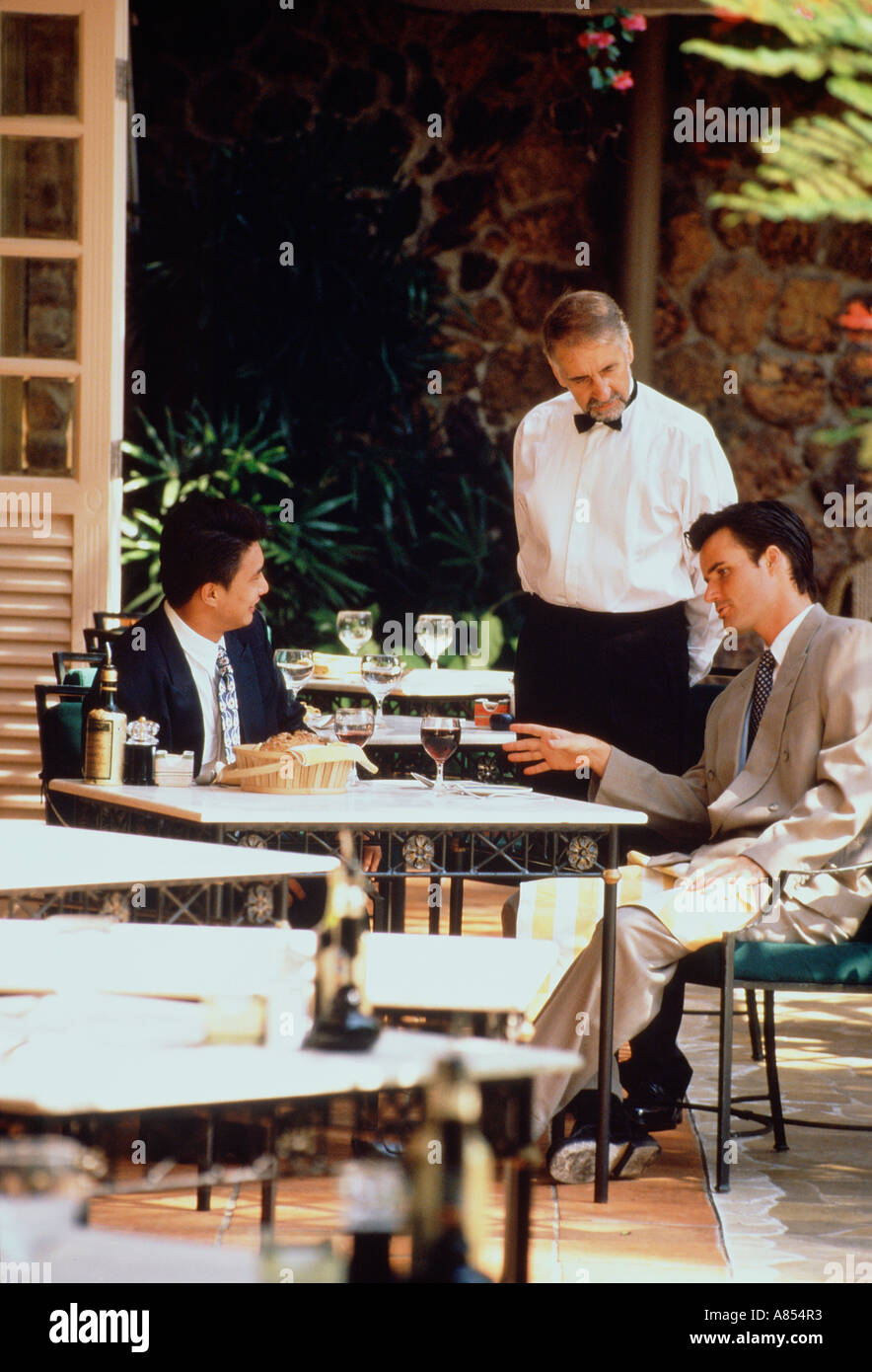 Zwei Männer sitzen am Tisch im Café im Freien mit Kellner sprechen. Stockfoto