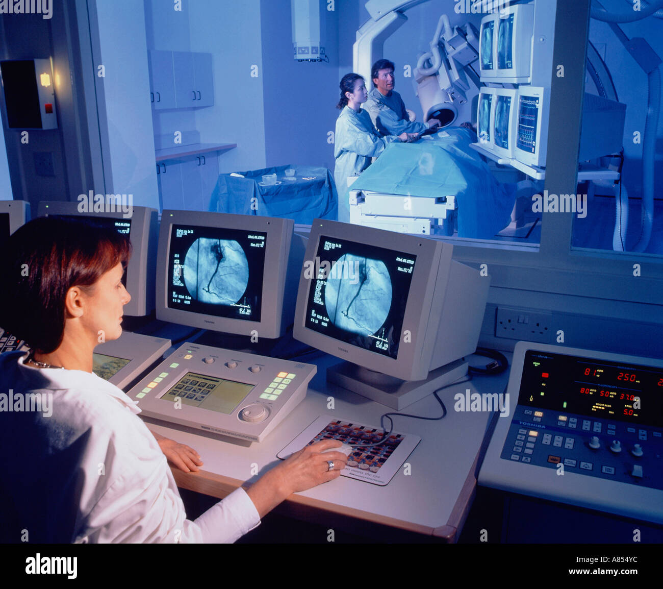 Krankenschwester in Computersteuerung Zimmer mit Blick auf Arzt und Krankenschwester mit Patienten im Krankenhaus Angiographie Scan Zimmer. Stockfoto