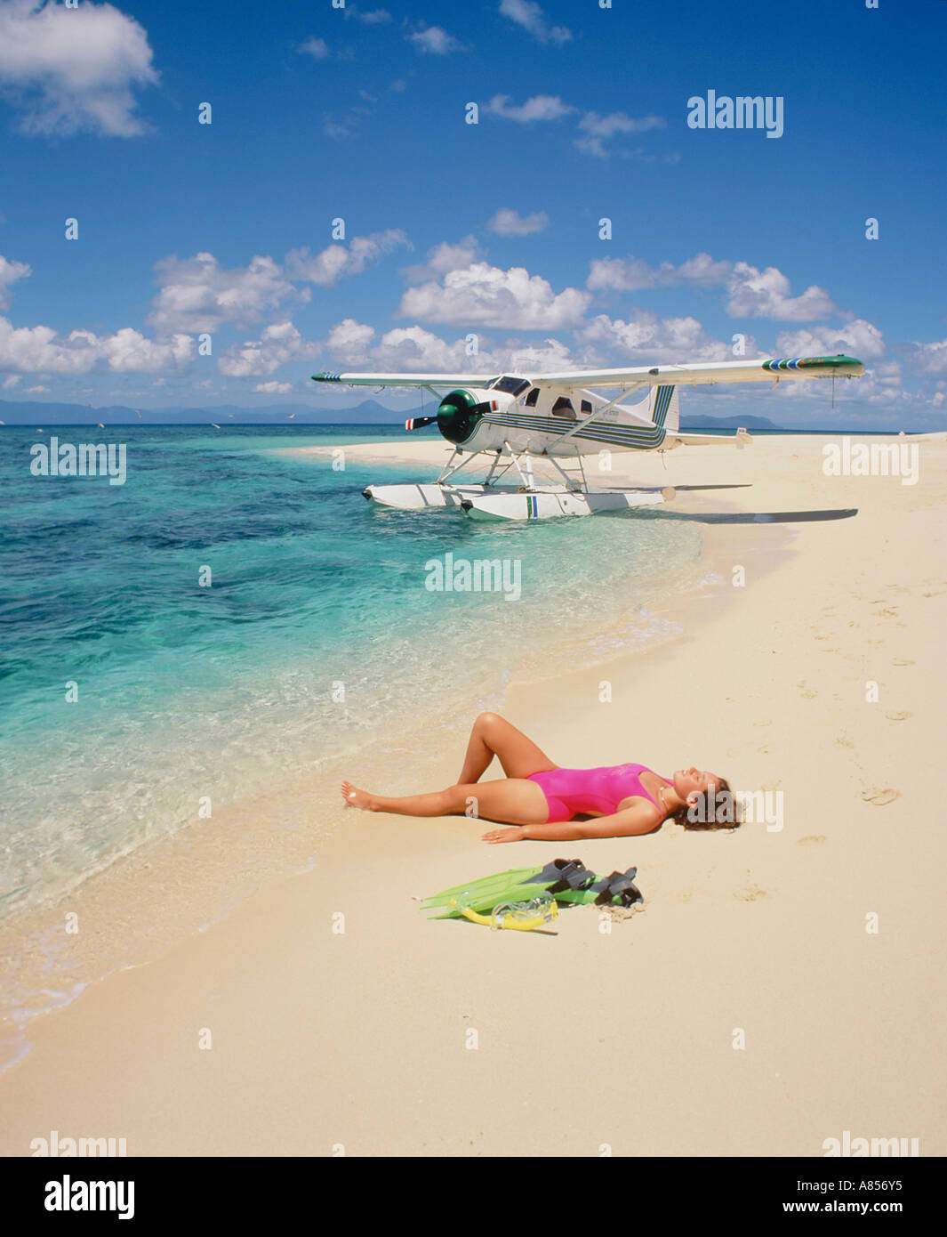 Junge Frau im Badeanzug liegend auf dem Rücken am Strand von Sudbury Cay, Queensland, Australien. Wasserflugzeug im Hintergrund. Stockfoto
