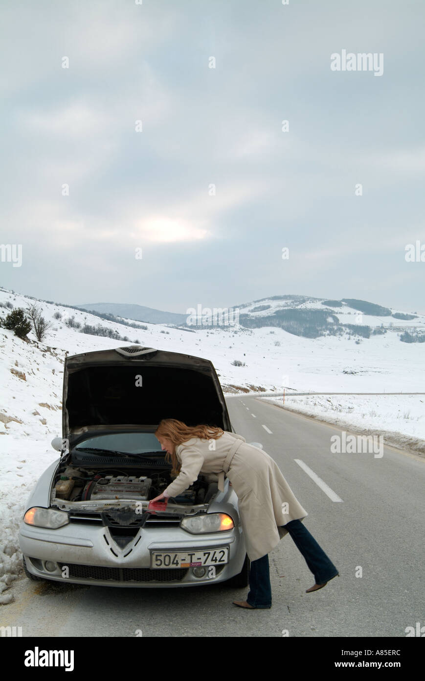 Junge Frau auf der Suche unter der Motorhaube des Her Auto nach gestrandet auf einer abgelegen Straße im Winter nach ein Break Down Stockfoto