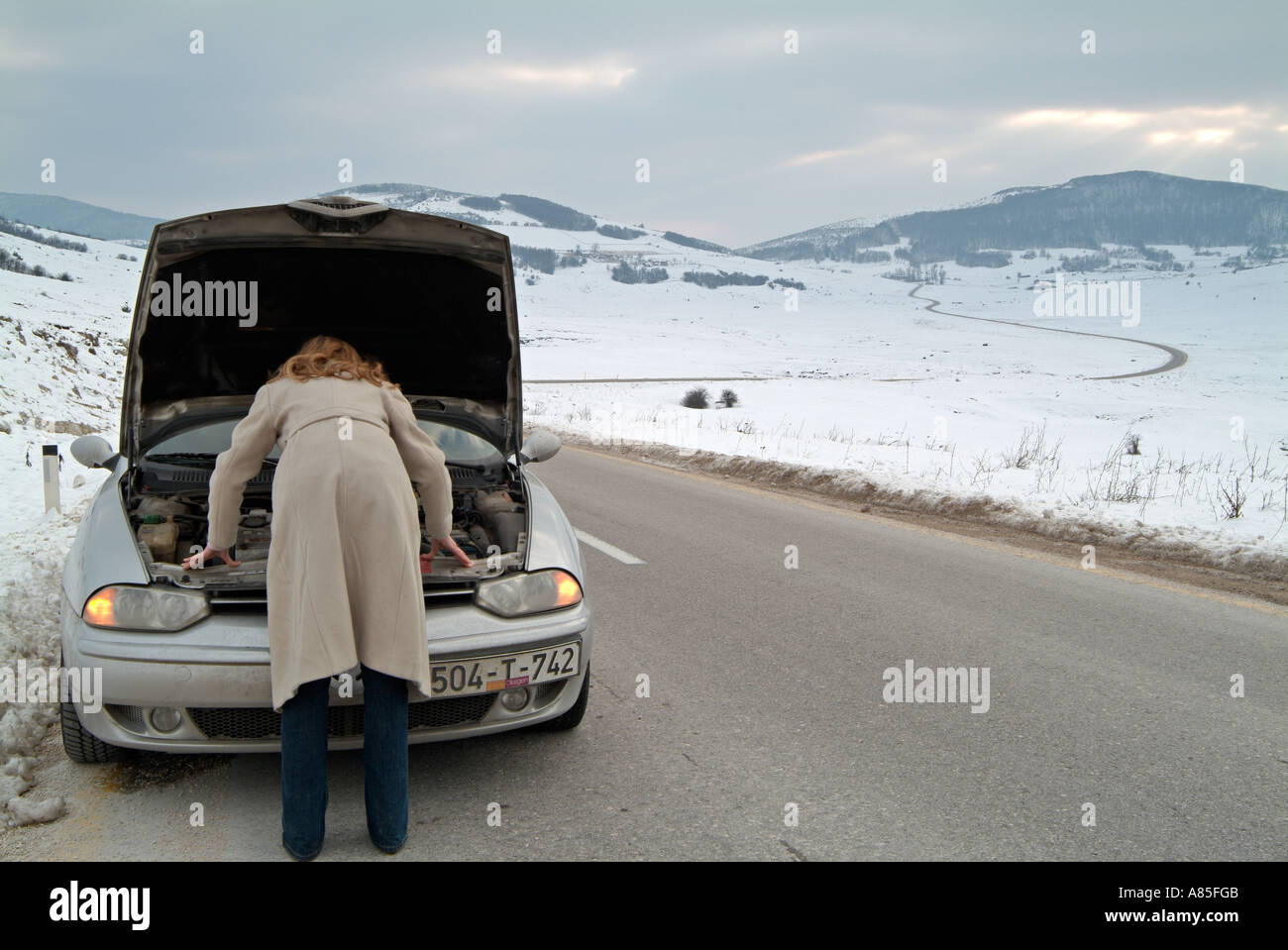 Junge Frau auf der Suche unter der Motorhaube des Her Auto nach gestrandet auf einer abgelegen Straße im Winter nach A Break Down Stockfoto