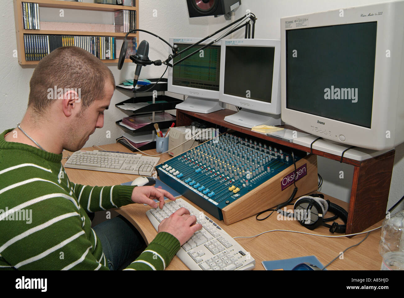Junge kaukasischen männlichen Sat an einem Computerarbeitsplatz im Produktionsstudio eine kommerzielle Radiostation Stockfoto