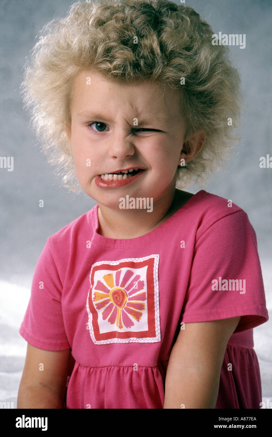 Ein kleines blondes Mädchen 4-6 jährige trägt ein rosa Kleid zwinkert ein lustiges Gesicht ziehen Gesichter hässlich Spaß machen Mund POV Herr Überfall Stockfoto