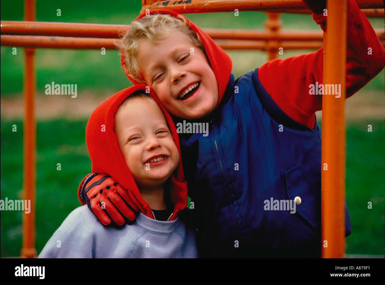 Zwei jungen in Handschuhe und Kapuzen-Sweatshirts umarmen und lachen beim Spielen im Freien auf einem Klettergerüst Stockfoto