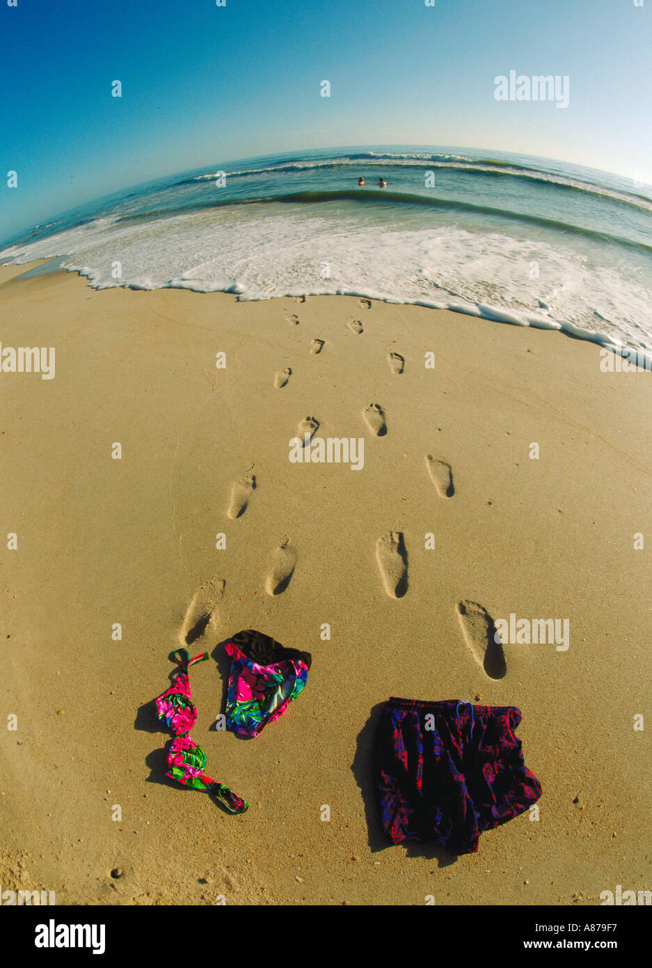 Mann und Frau Baden Anzüge lag in den Sand mit Fußspuren führen ins Wasser als sie skinny dip in der Ferne Stockfoto