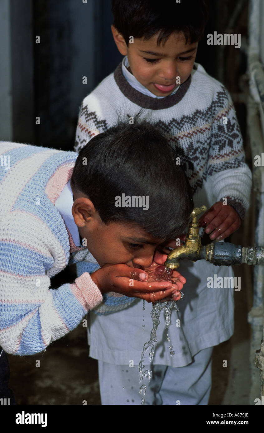 Schüler, die Wasser aus einem Wasserhahn in ihrem Schulhof trinken. Quetta, Pakistan Stockfoto
