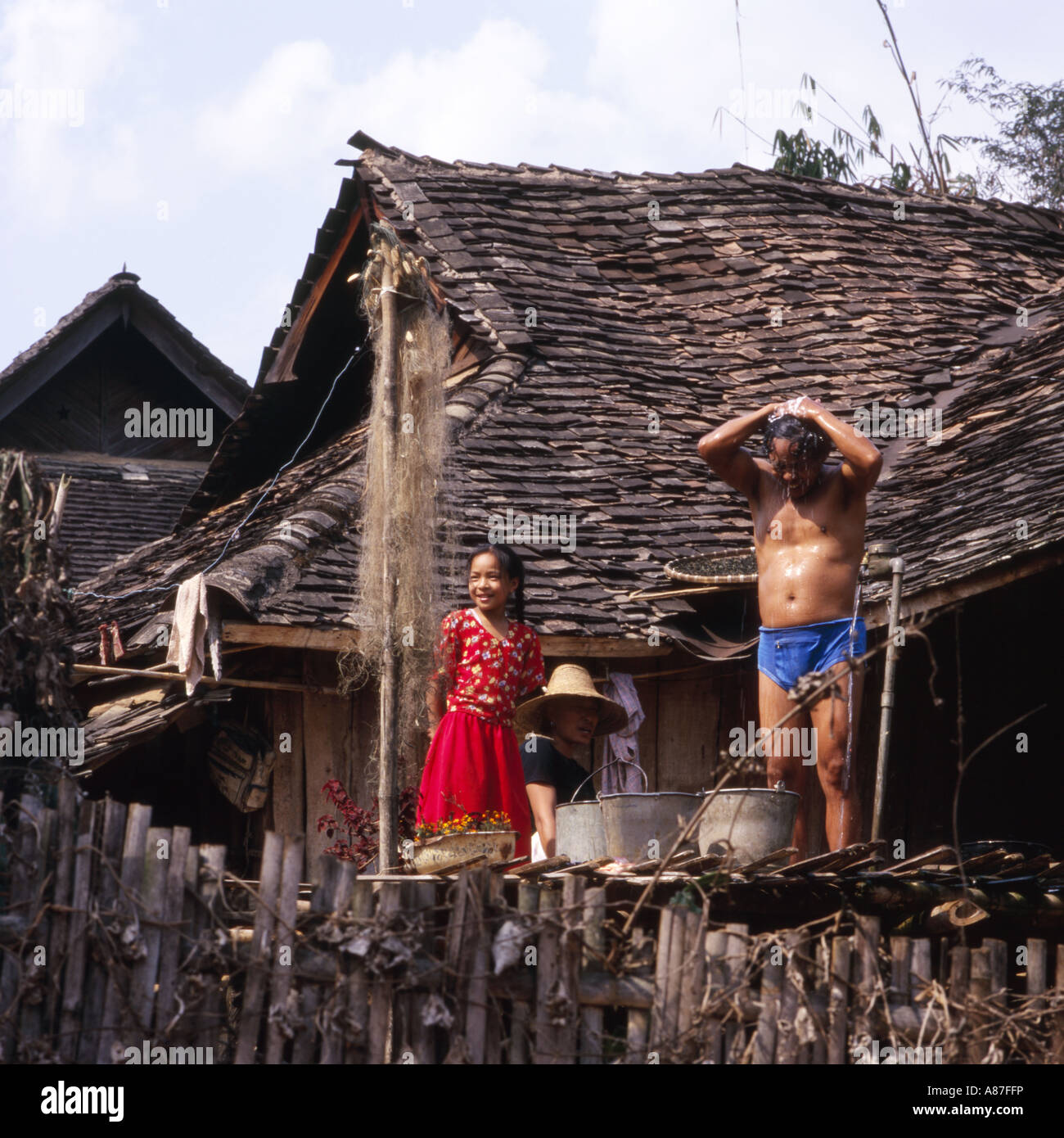 Lokale Mann unter der Dusche vom Standrohr vor seinem Haus, Familie auf, in der Nähe von Jinghong, China Stockfoto